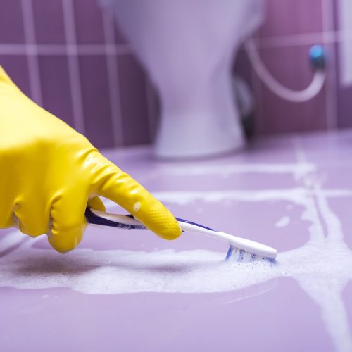 Hand in yellow glove cleans the tile toothbrush.